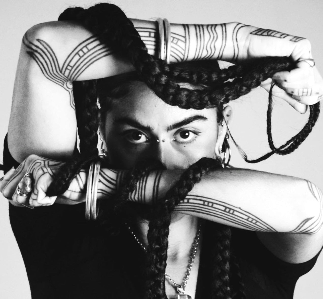 Black and white portrait of a person with braided hair and tattoos on arms.
